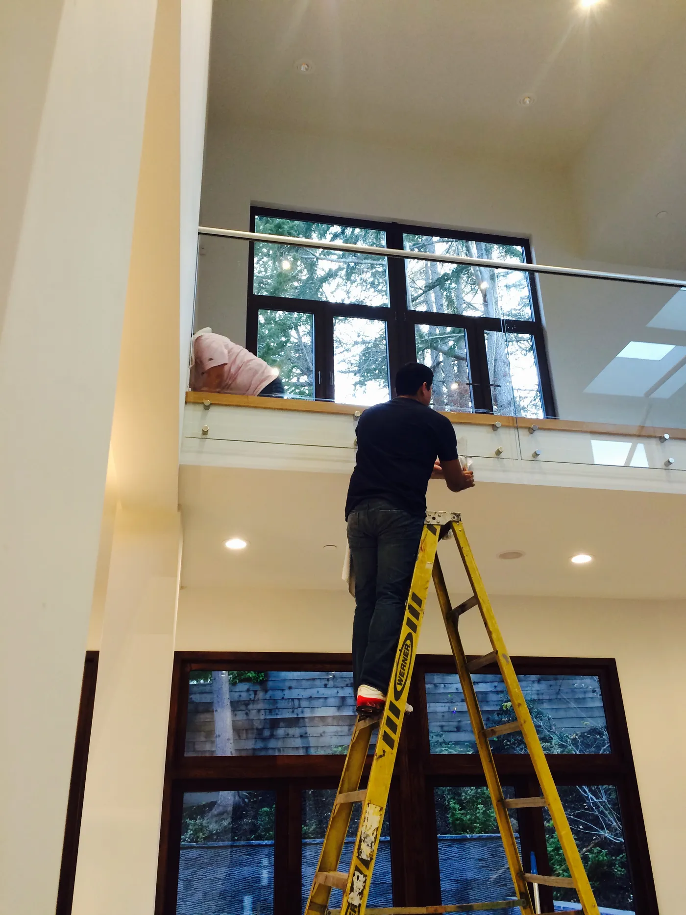 White Flowers team member cleaning high windows on a ladder in a modern Peninsula home