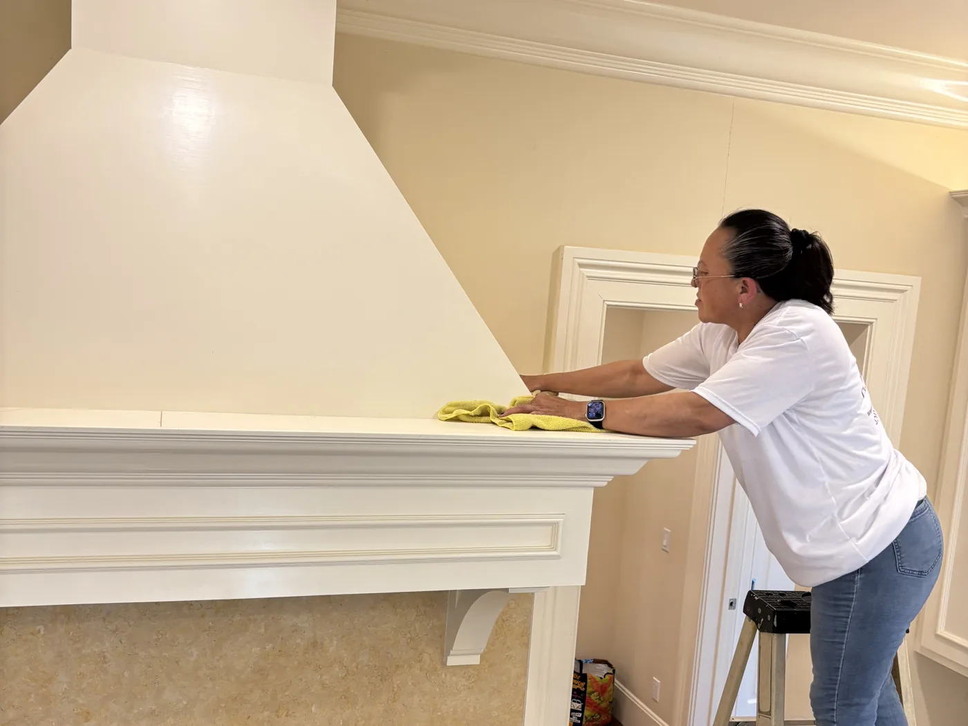 A White Flowers cleaner wiping down a range hood in a kitchen being finished after a remodel