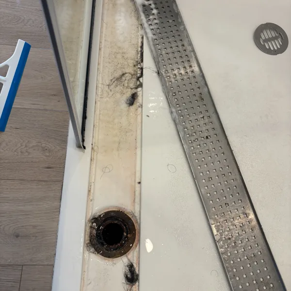 Linear shower drain lifted out, showing hair and dark buildup packed into the channel underneath