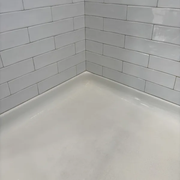 The same shower corner after cleaning, with white grout lines and a clean pan