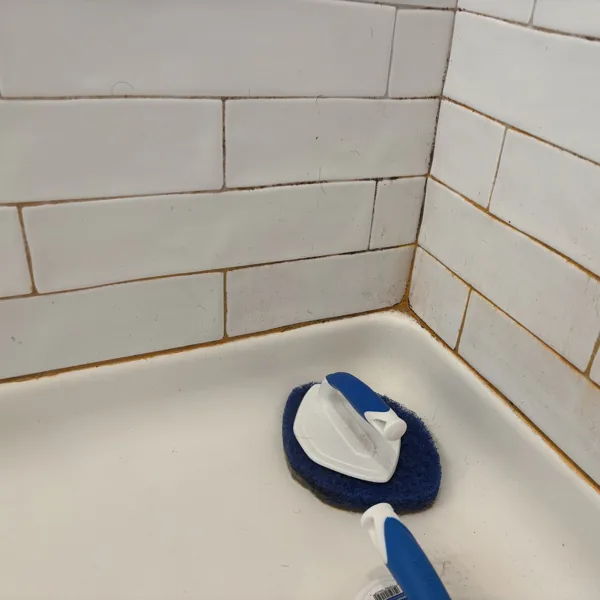 Shower corner with orange staining through the grout lines and along the base before cleaning
