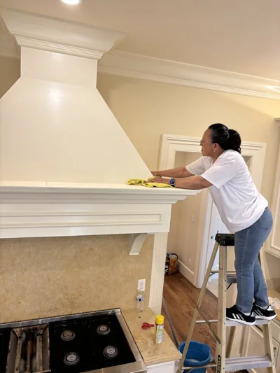 A White Flowers cleaner on a step stool wiping down a range hood in a kitchen being finished